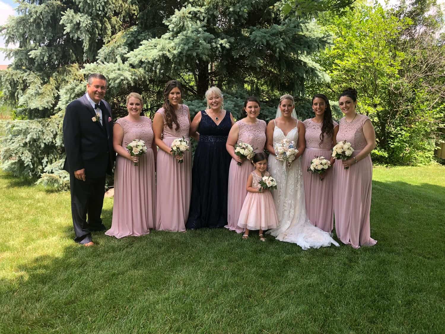 Wedding party with bride, groom, and bridesmaids outdoors in garden.