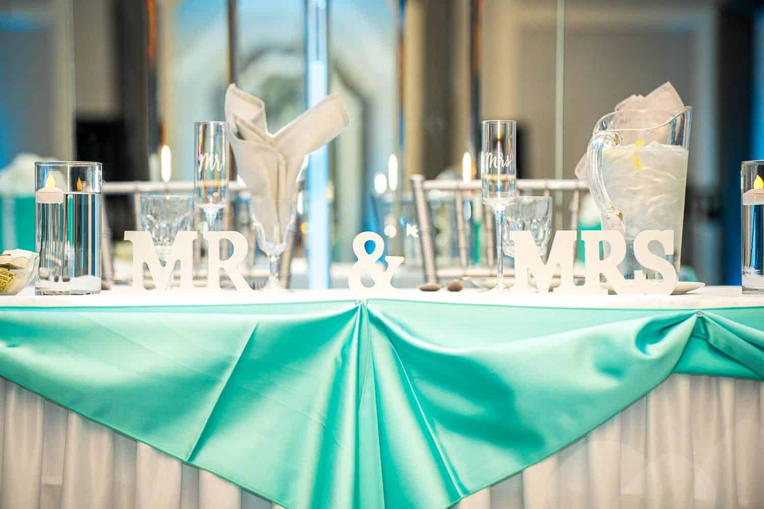 Elegant wedding reception table with Mr. & Mrs. signs and turquoise tablecloth.